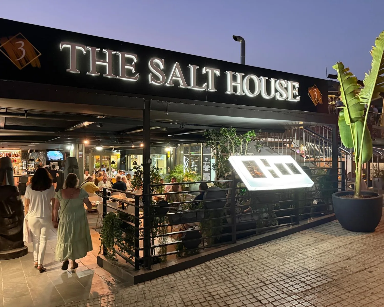 G&auml;ste betreten The Salt House in der Abendd&auml;mmerung, unter dem beleuchteten Schild