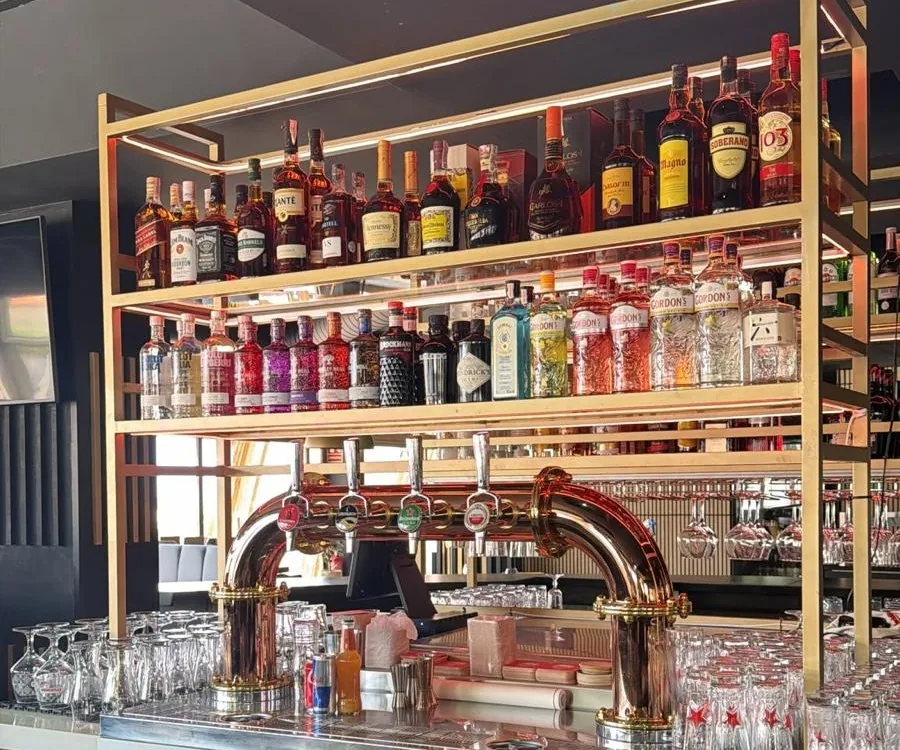 La barra: estanter&iacute;as doradas llenas de botellas sobre los grifos de cerveza