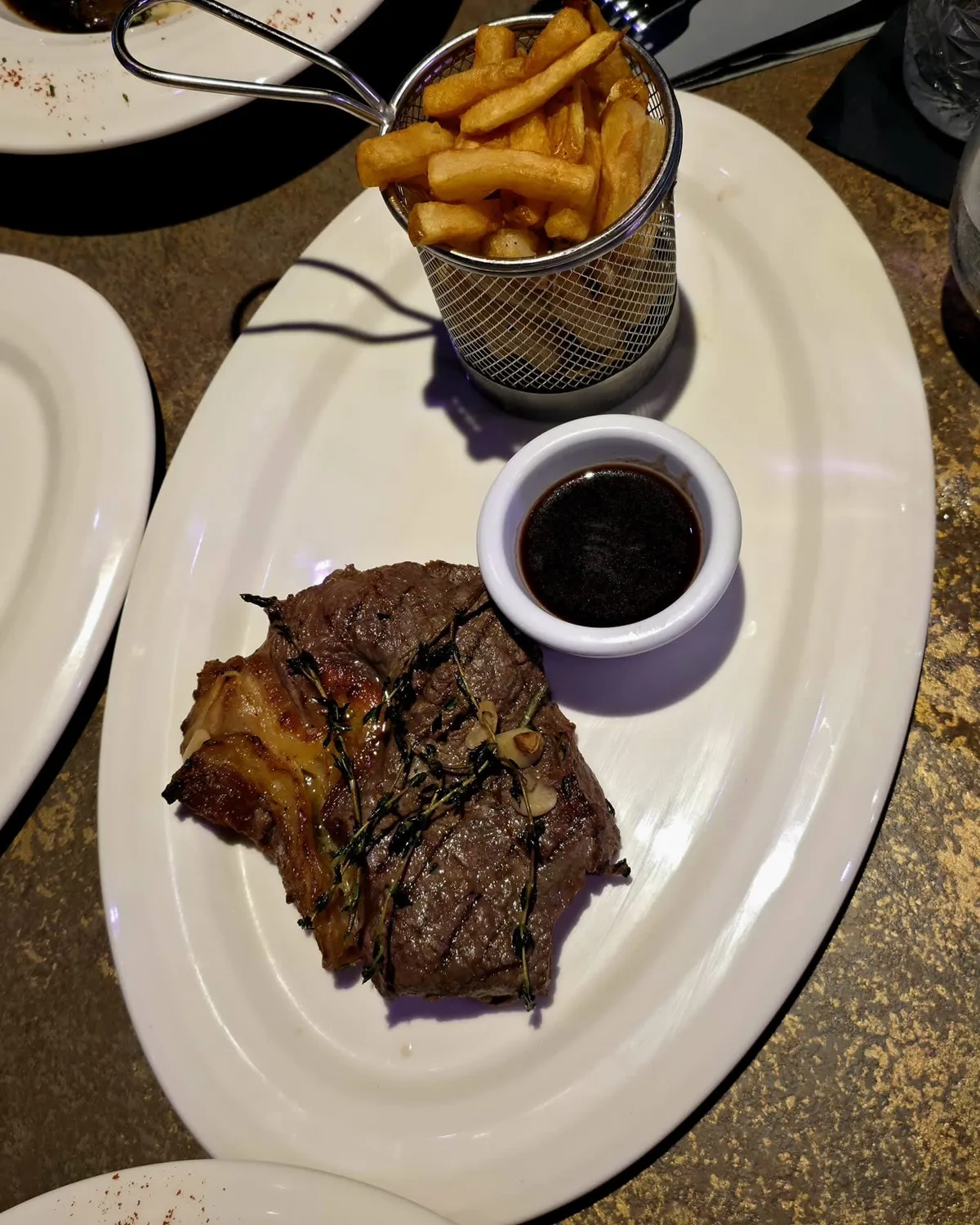 A grilled steak with a pot of sauce and a basket of fries