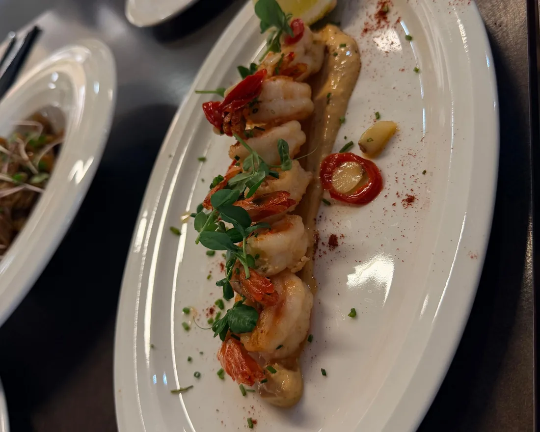 Peeled prawns on a long plate with herbs and a roasted cherry tomato