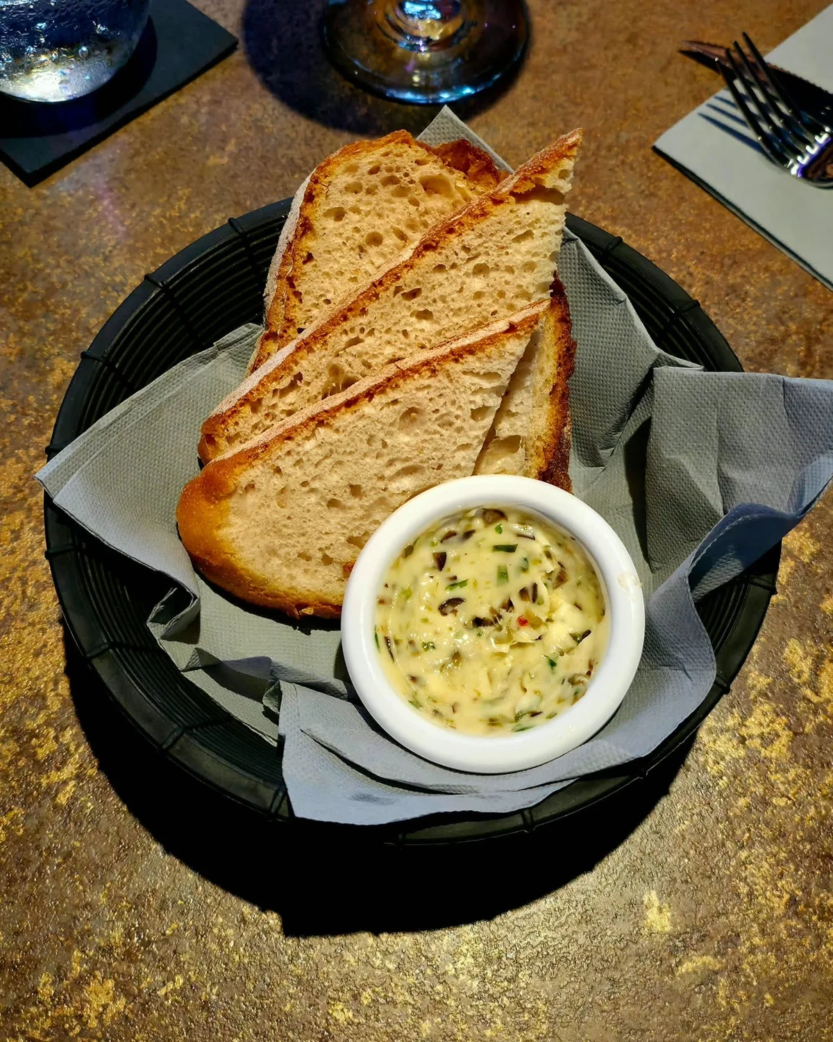 Slices of sourdough in a paper-lined basket, with a pot of butter flavoured with olives and herbs