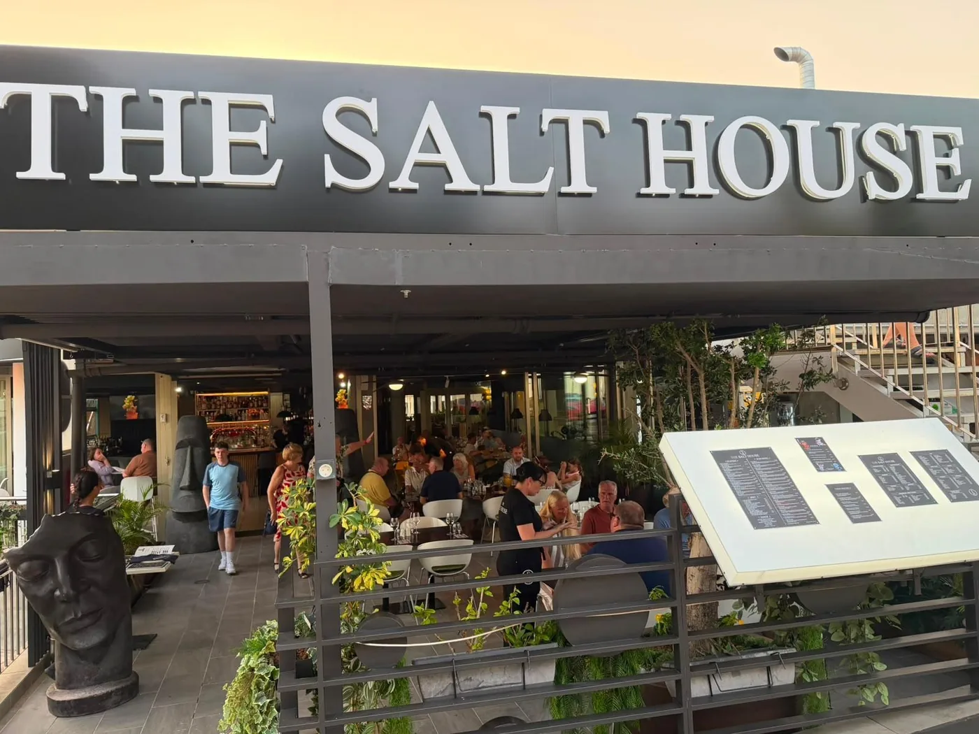 Clientes cenando en la terraza al anochecer, bajo el gran r&oacute;tulo de The Salt House
