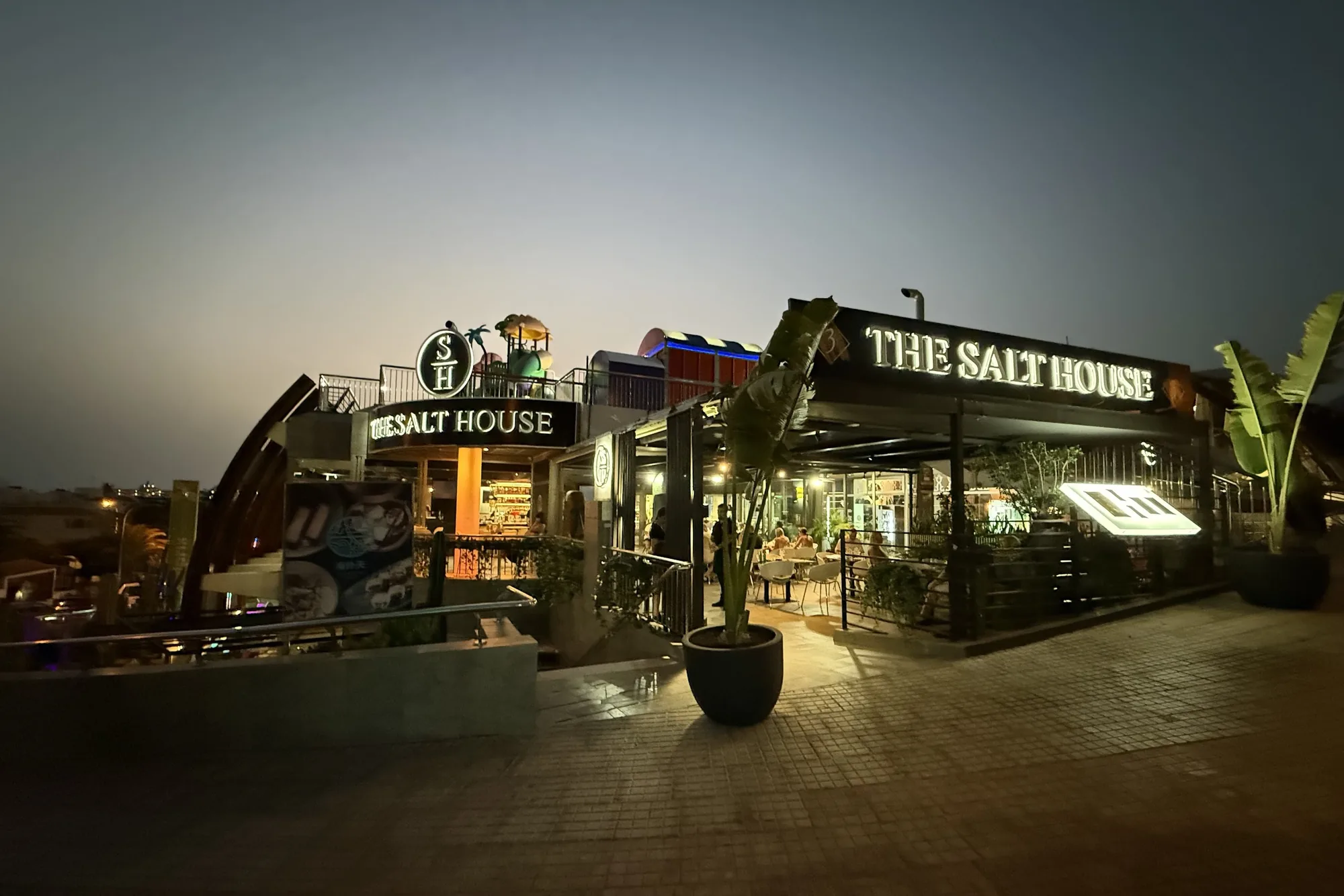 The Salt House de noche: el rótulo iluminado, la terraza y las plantas de la fachada